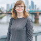 Hier sieht man Yasmin Schulze. Im Hintergrund ist verschwommen der Main in Frankfurt zu erkennen. Sie steht auf einer Brücke über dem Fluss.